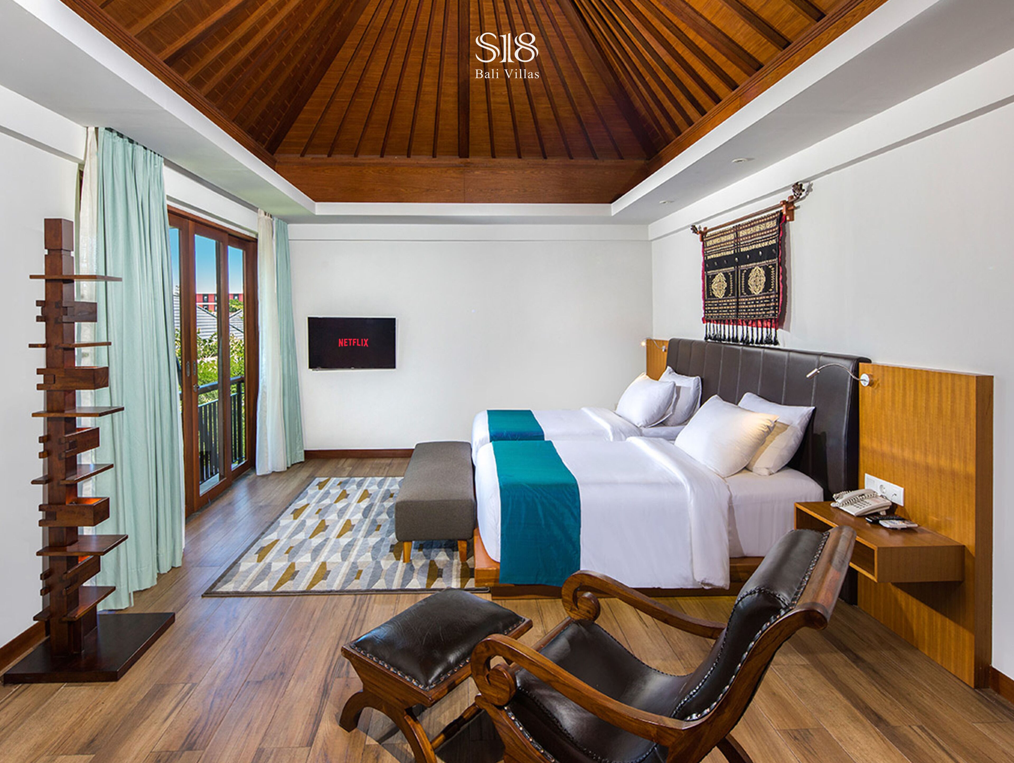 Una habitación de hotel moderna con techo de madera, una cama con colcha azul y blanca, un televisor en la pared y una mesita de noche de madera.