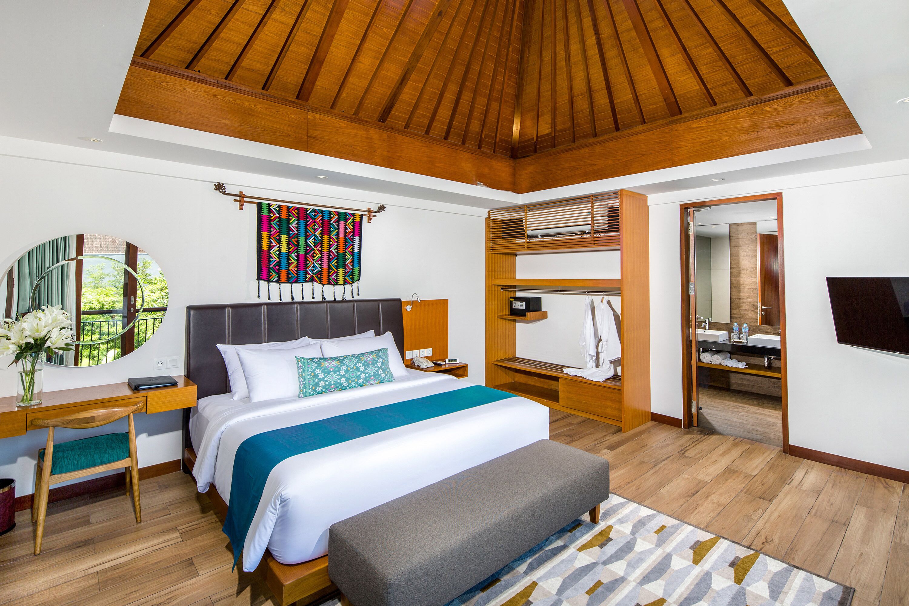 Une chambre spacieuse avec un grand lit, un plafond en bois, un bureau avec une chaise, une table de chevet et un miroir.