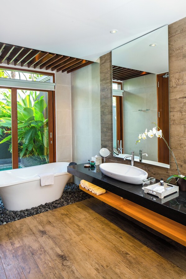 Un baño moderno con una bañera independiente, un espejo grande y un mueble de tocador de madera.