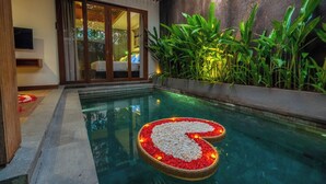 Una piscina con un arreglo en forma de corazón de guijarros blancos y flores rojas, rodeada de exuberante follaje verde.
