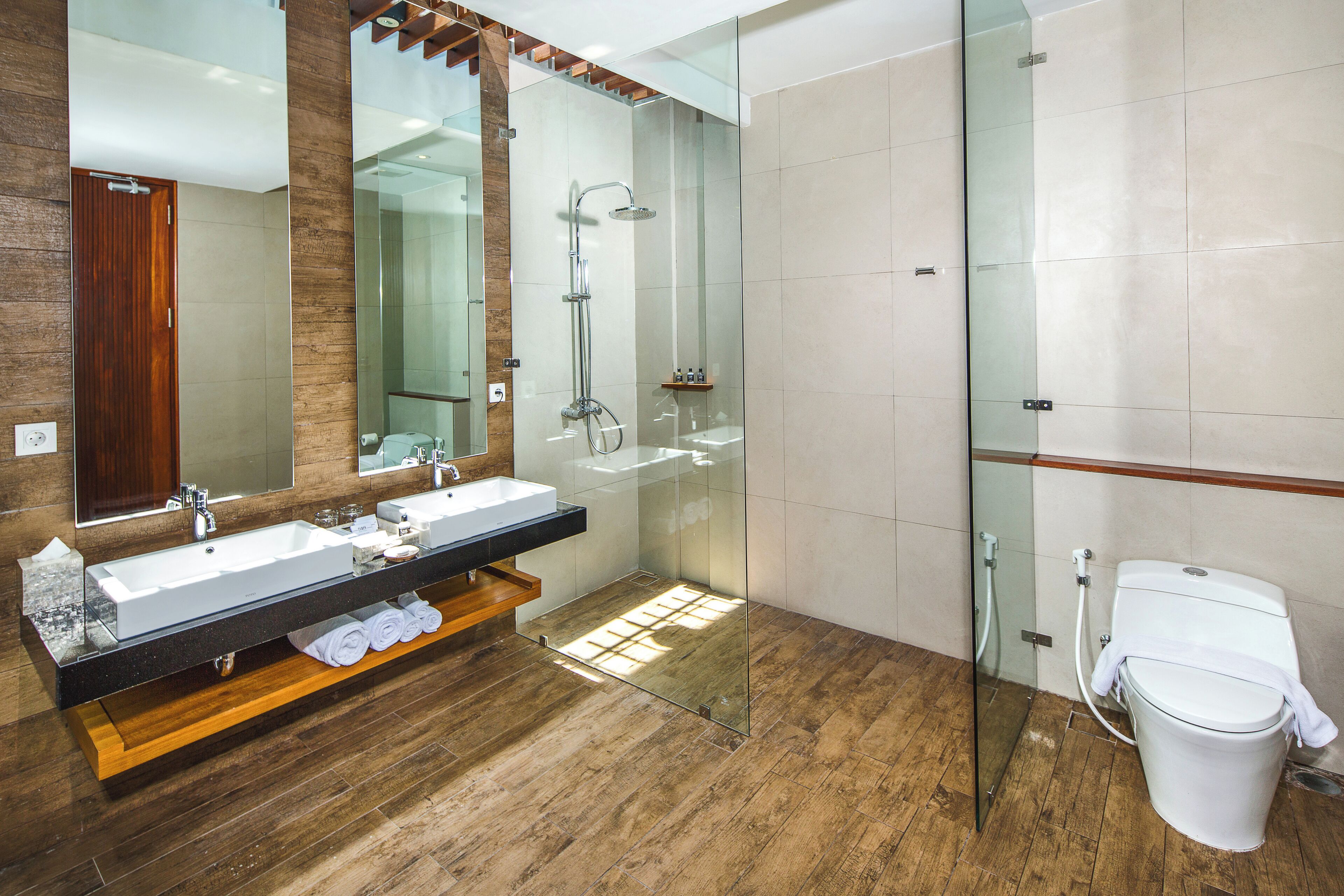 Un baño moderno con un mueble de tocador de madera, un espejo grande, ducha con cerramiento de vidrio y un inodoro blanco.