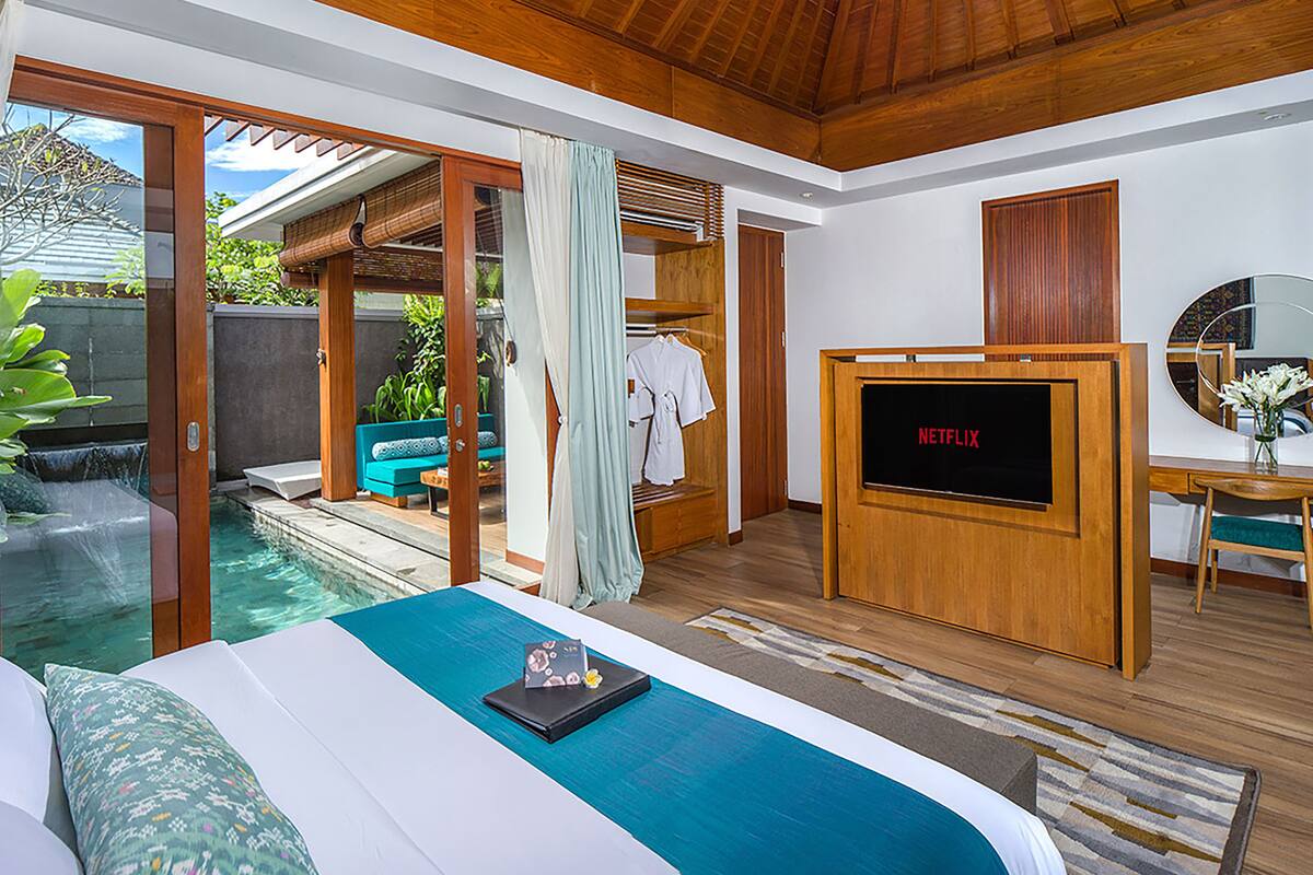 Une chambre d’hôtel moderne dotée d’un grand lit, d’une télévision, d’un petit bureau et offrant une vue sur l’espace extérieur de la piscine.