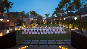 Montaje de boda al aire libre con mesas dispuestas en forma de semicírculo, rodeado de palmeras y una estructura decorativa circular.