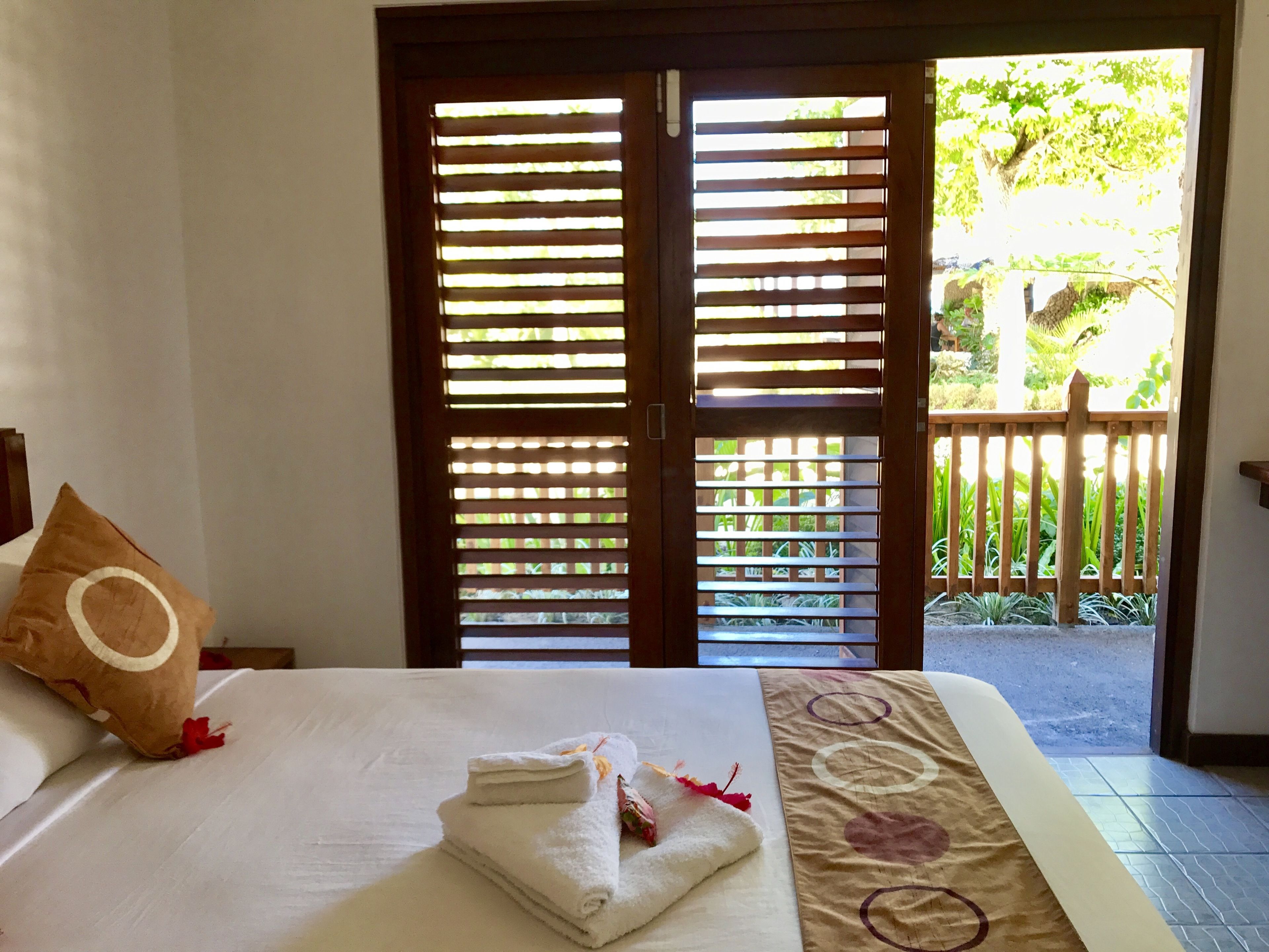 Habitación de hotel con cama, almohada y vista a un jardín a través de una puerta de madera.