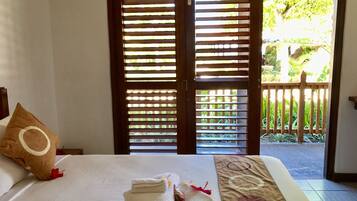 Habitación de hotel con cama, almohada y vista a un jardín a través de una puerta de madera.