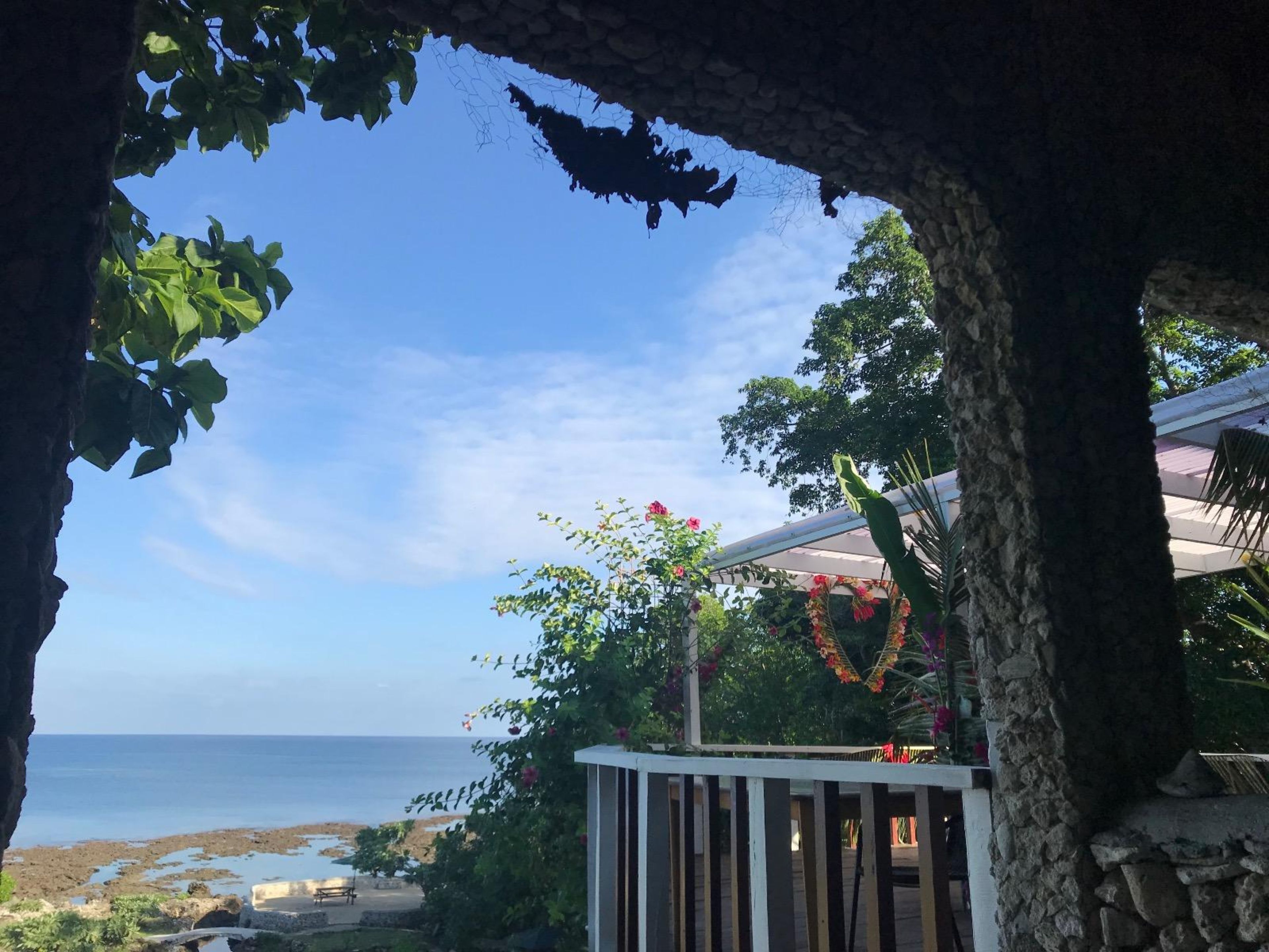 Vista costera con una estructura de piedra, una terraza de madera y cielo despejado.