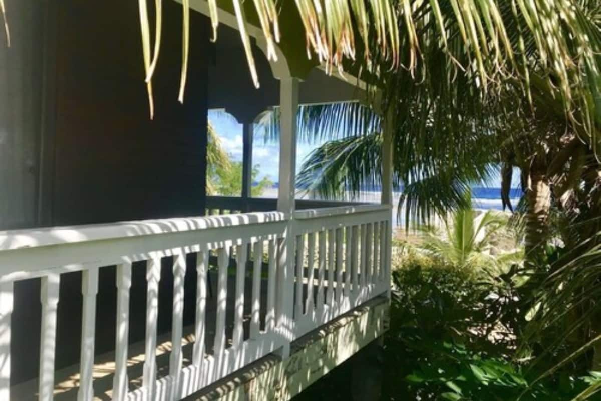 A balcony with a white railing overlooking a tropical garden and a view of the ocean.