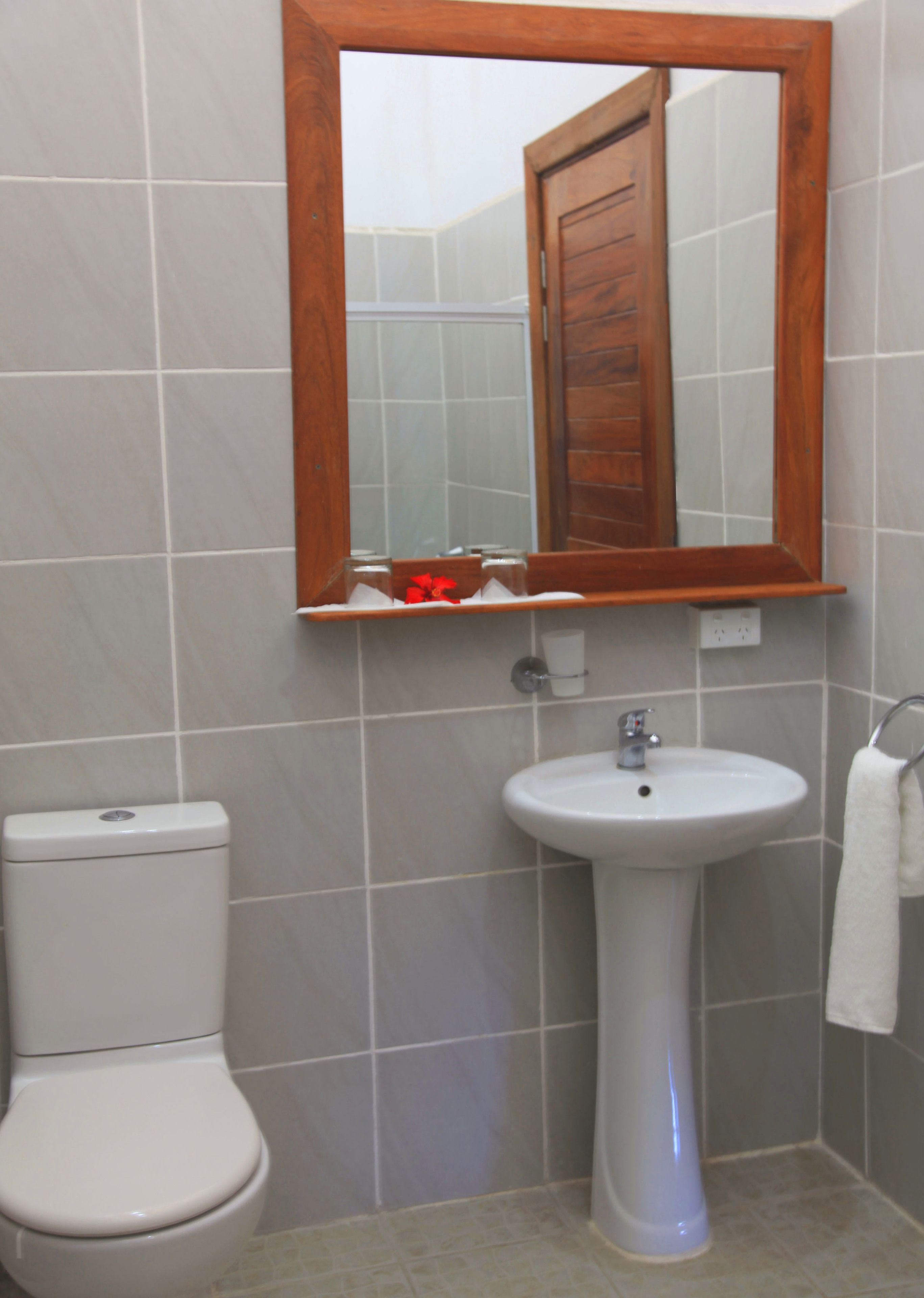 A bathroom with a white toilet, a pedestal sink, and a wooden-framed mirror.