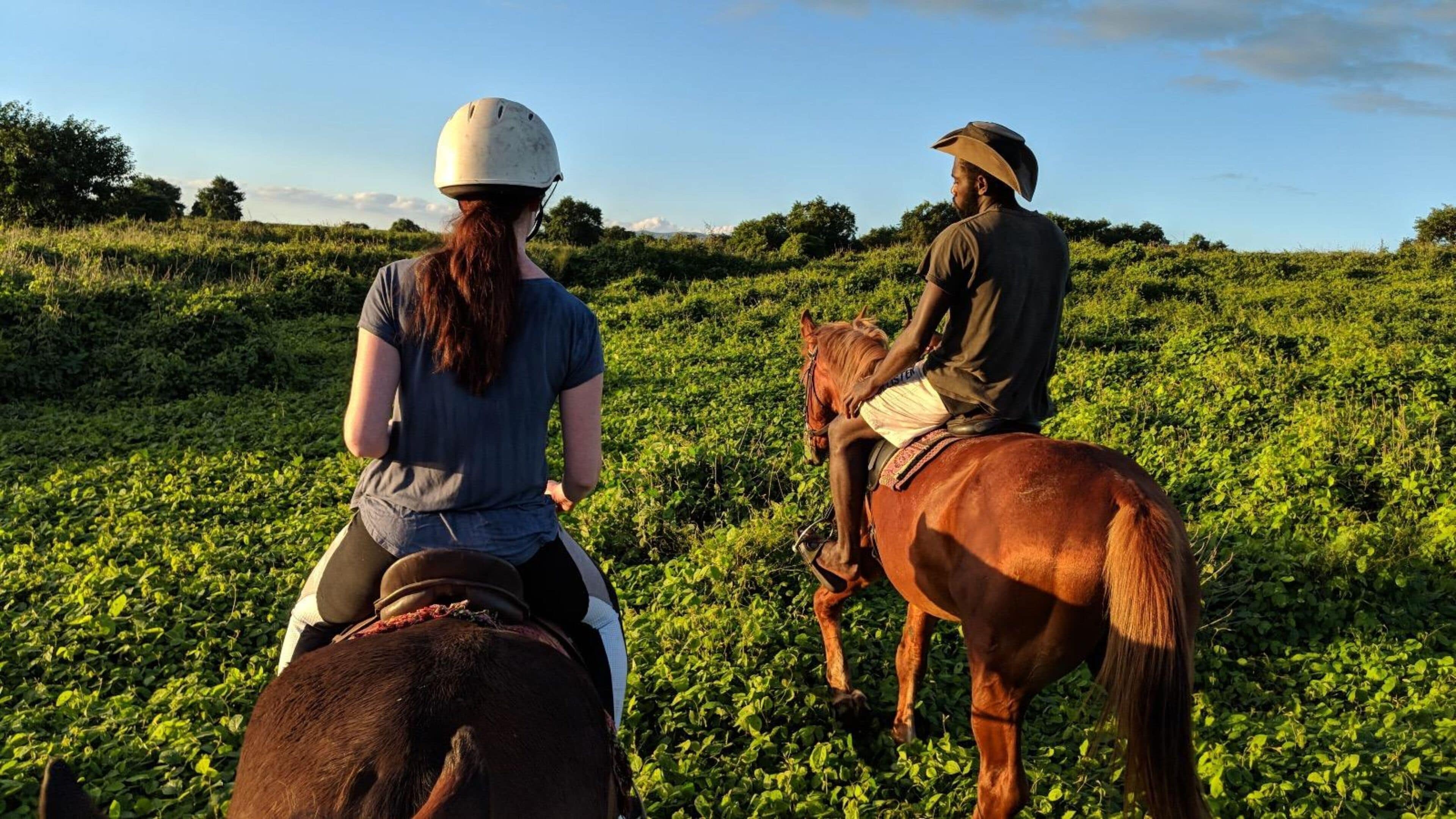Dos personas montando a caballo en un campo con vegetación abundante.