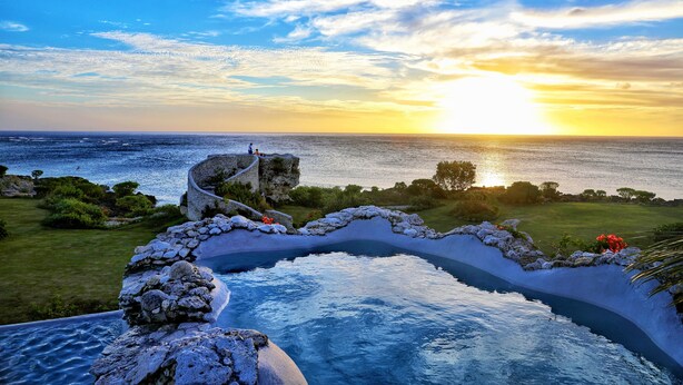 A pool with a stone pathway and a view of the ocean at sunset. - Tanna Evergreen Resort & Tours (Tanna Island)