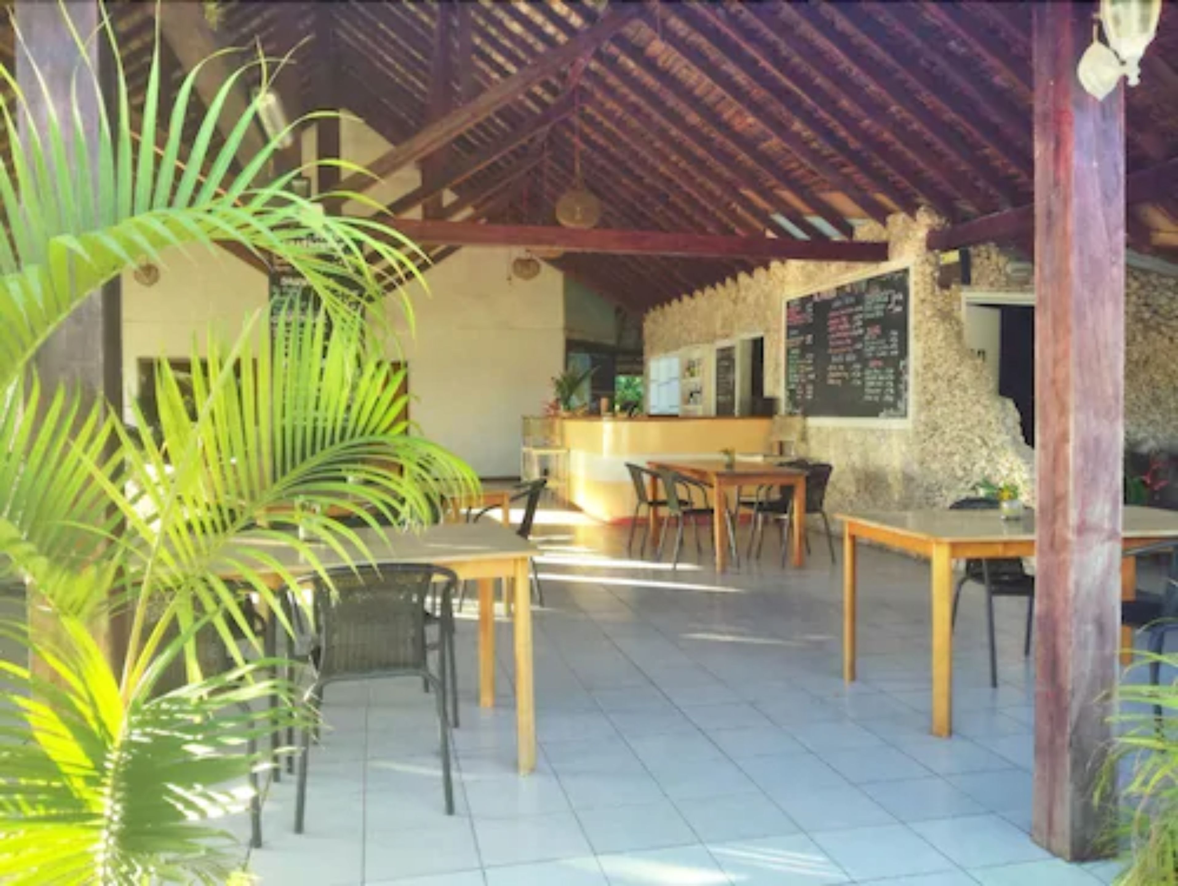 Un área de comedor al aire libre con mesas y sillas de madera, rodeada de plantas en macetas.