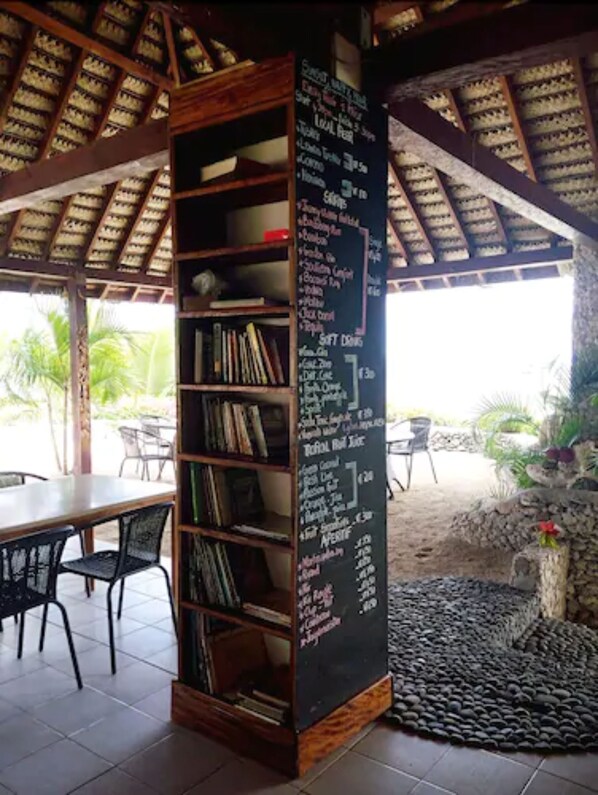 Un espacio de estar al aire libre cubierto con una estantería de madera y un menú en pizarra que ofrece opciones de comida y bebida.