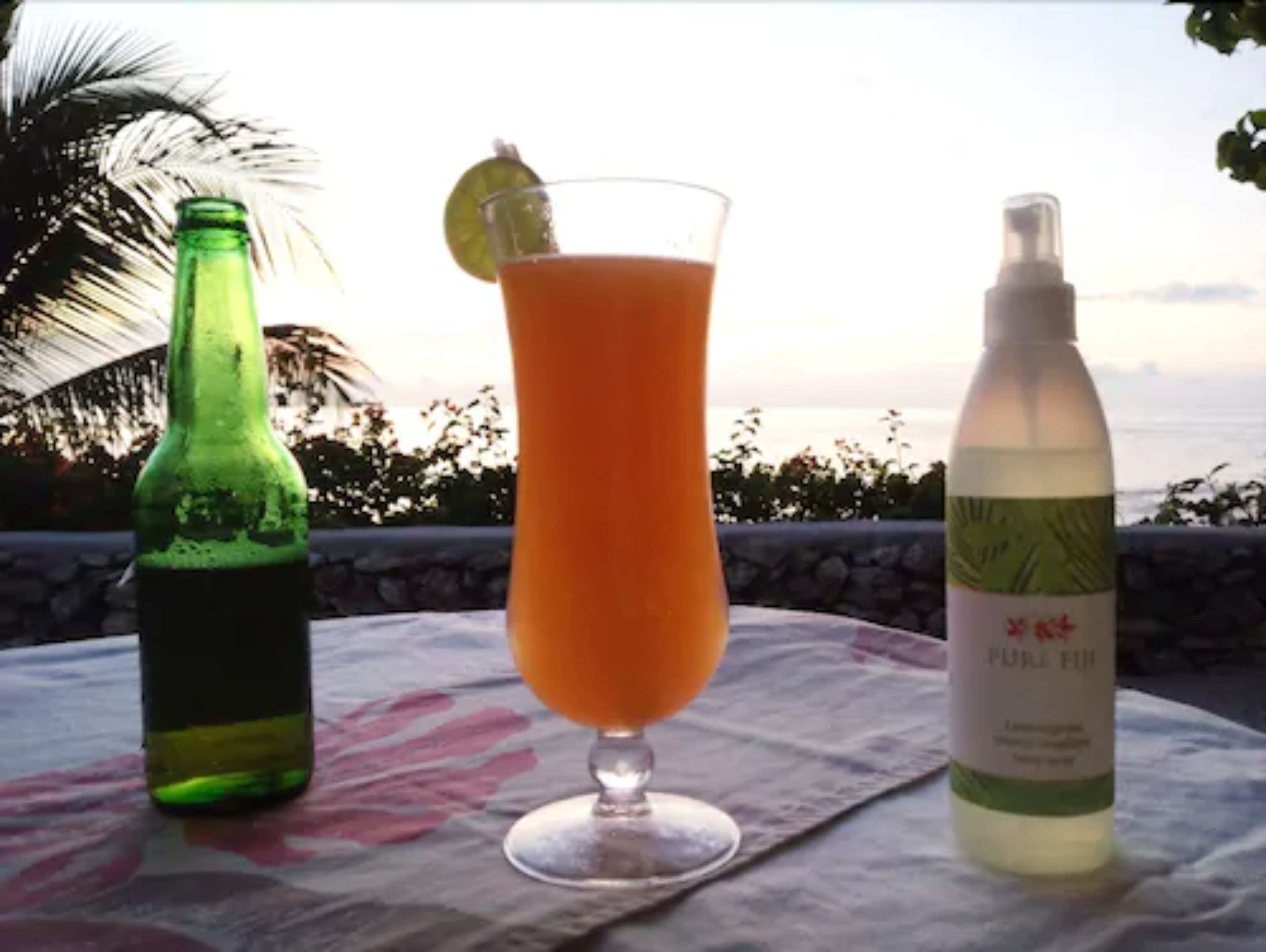 Een tafel met een glas sinaasappelsap, een groene fles en een witte fles met etiket.