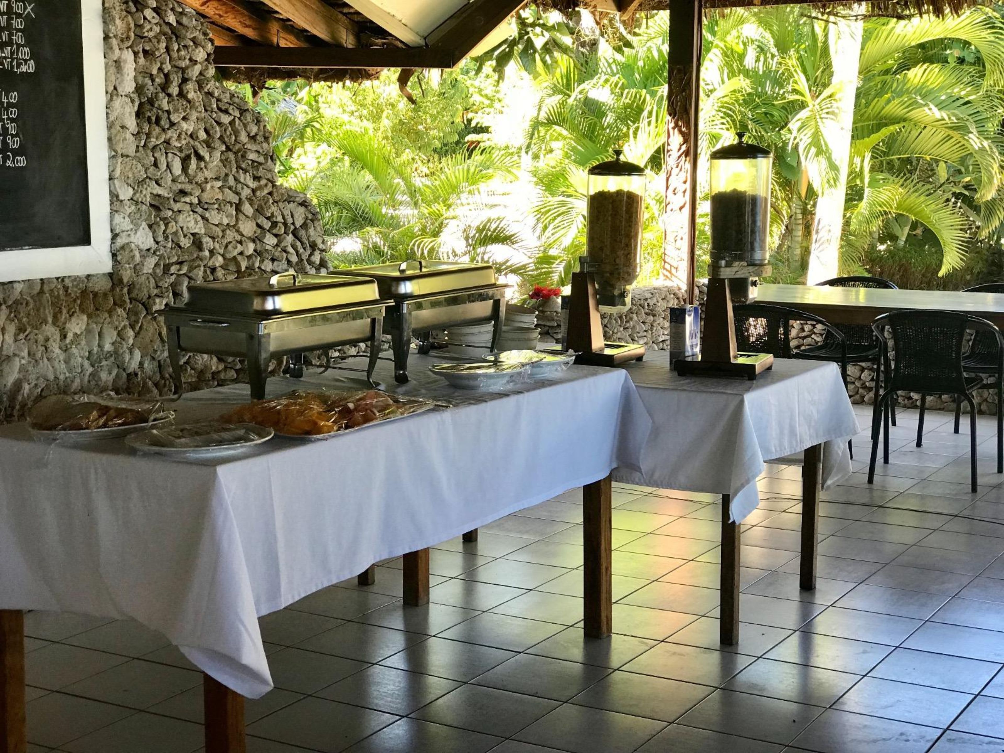 Buffet montado com várias estações de serviço, parede de pedra e ambiente tropical ao ar livre.