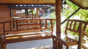 Una terraza de madera con bancos y barandilla, rodeada de follaje.