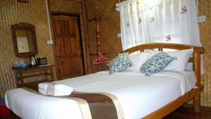 Una cama de madera con ropa de cama blanca, una mesita de noche de madera con una tetera y tazas, y una puerta de madera en una habitación con papel tapiz estampado.