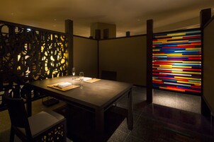 Un comedor moderno con una mesa larga, sillas y un panel decorativo con un diseño geométrico.