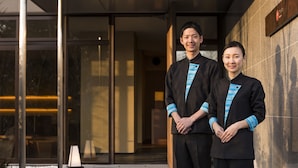 Two individuals standing in front of a building with a glass entrance and a stone wall. - Hoshino Resorts KAI Anjin (Ito)