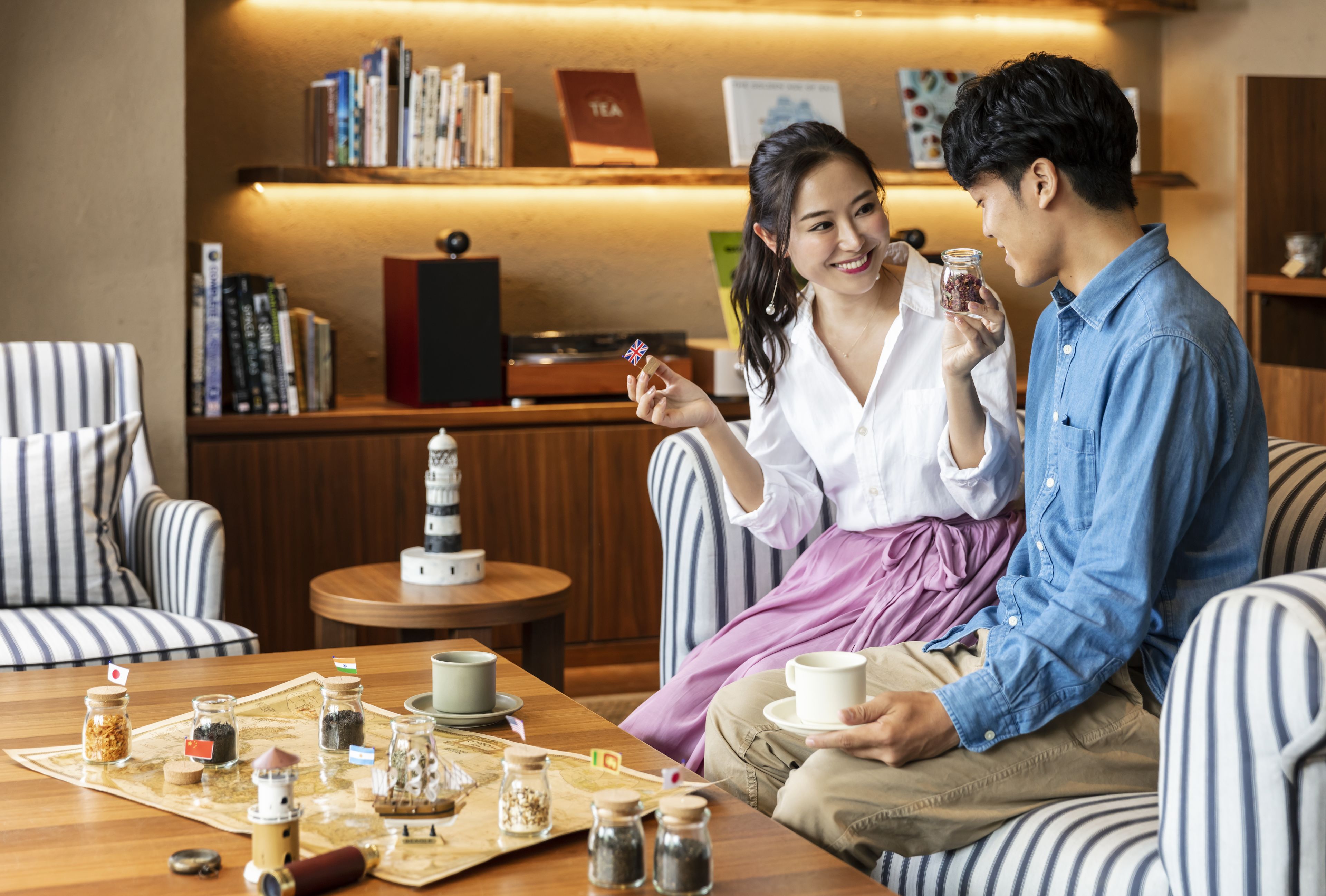 A cozy seating area with striped chairs, a wooden table with tea and snacks, and a bookshelf in the background.