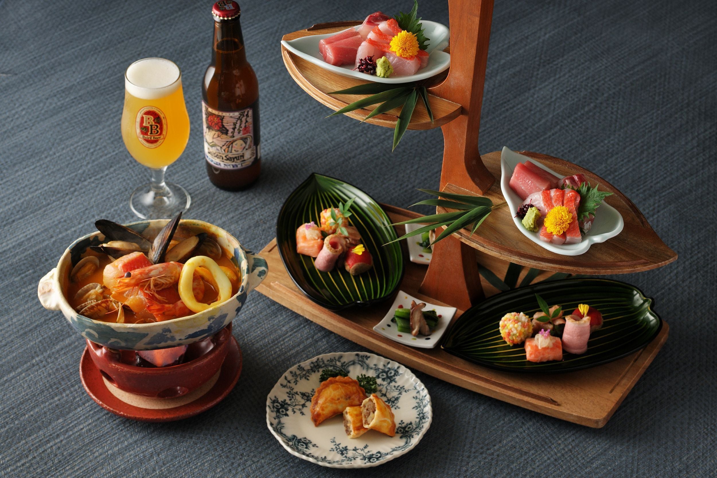 A variety of Japanese dishes including sushi, sashimi, and a bowl of seafood stew, served on wooden trays and plates.