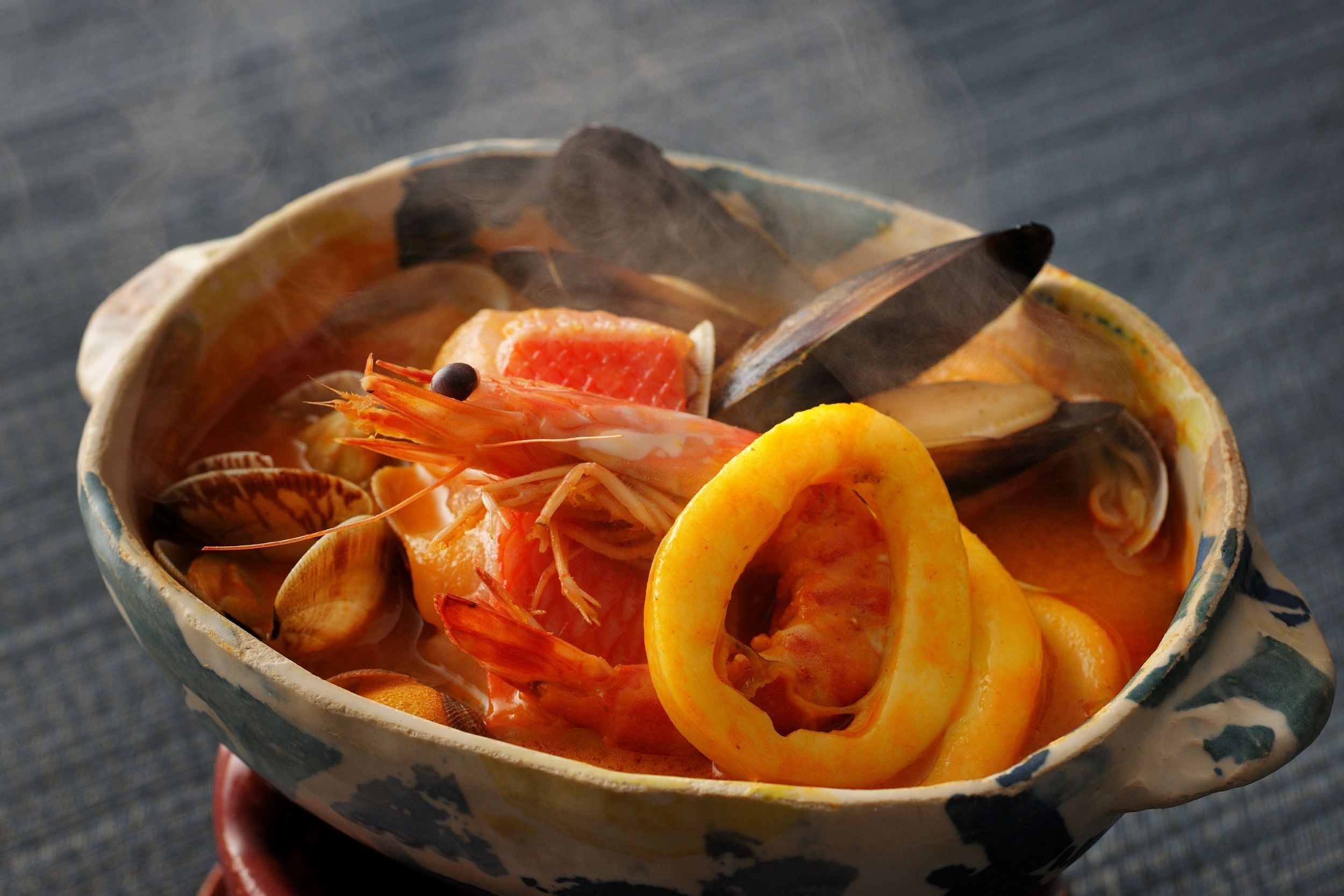 A bowl of seafood stew with clams, shrimp, and a slice of lemon.