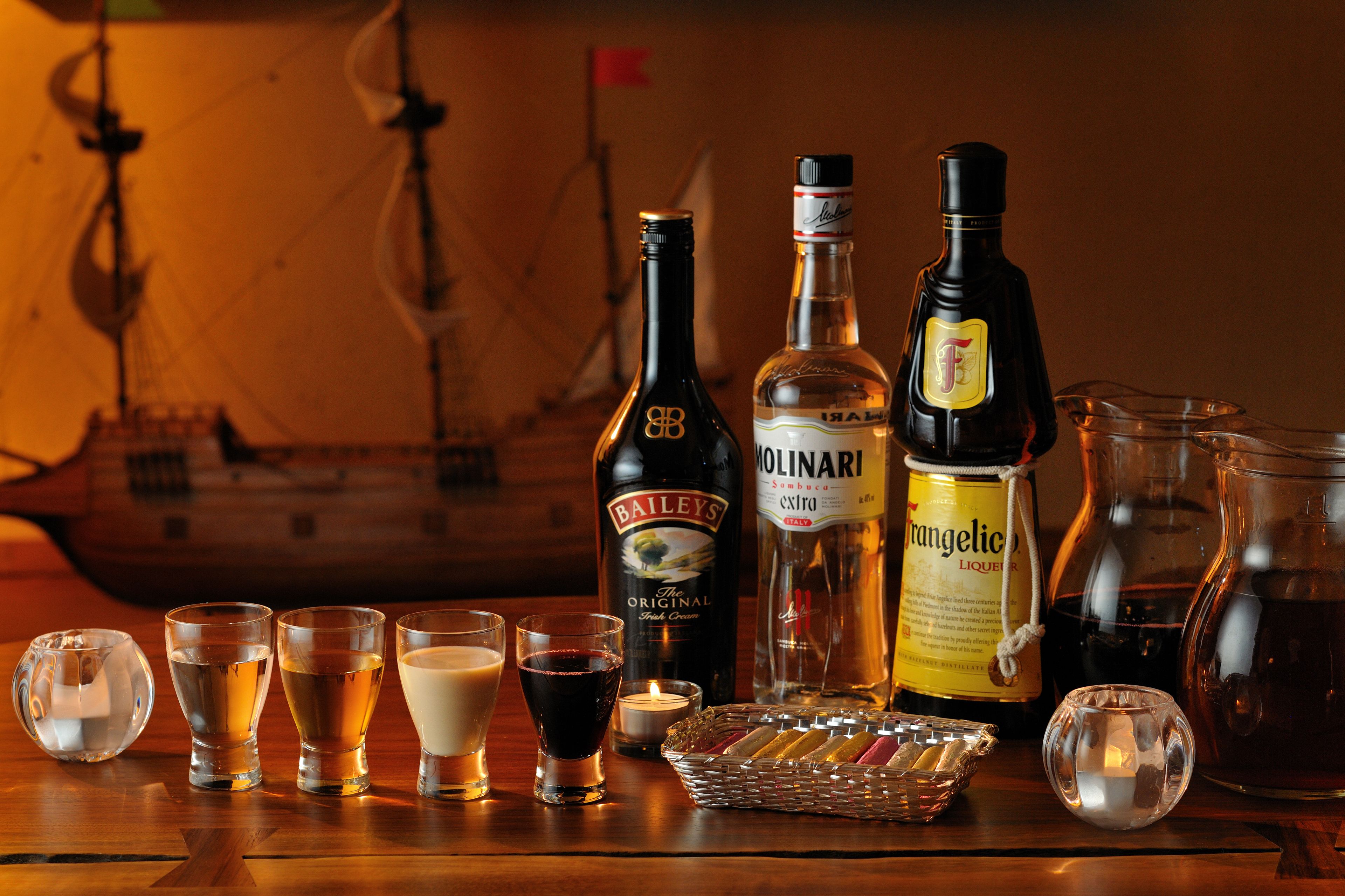 Ett träbord med olika flaskor och glas med drycker, en modell av ett skepp och ett ljus.