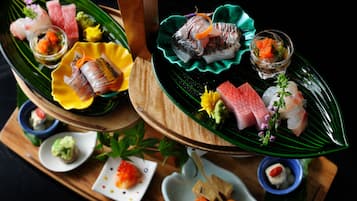 A multi-tiered serving dish with various types of sushi and sashimi, garnished with small flowers and vegetables.