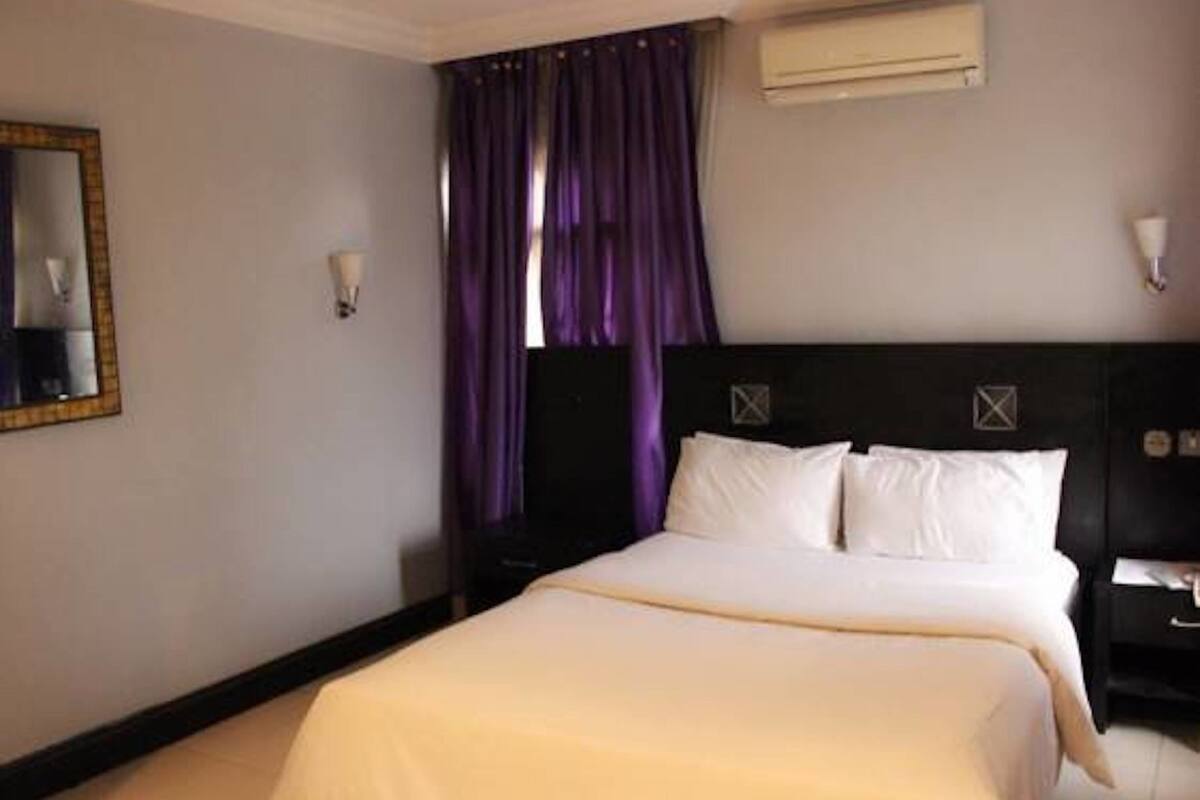 A hotel room with a bed, a nightstand, a mirror, and an air conditioning unit.