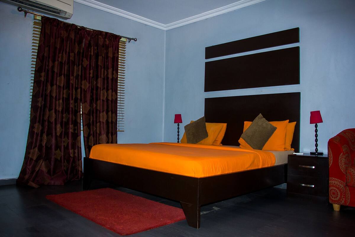 A bedroom with a bed, a nightstand, a red chair, and a window with curtains.