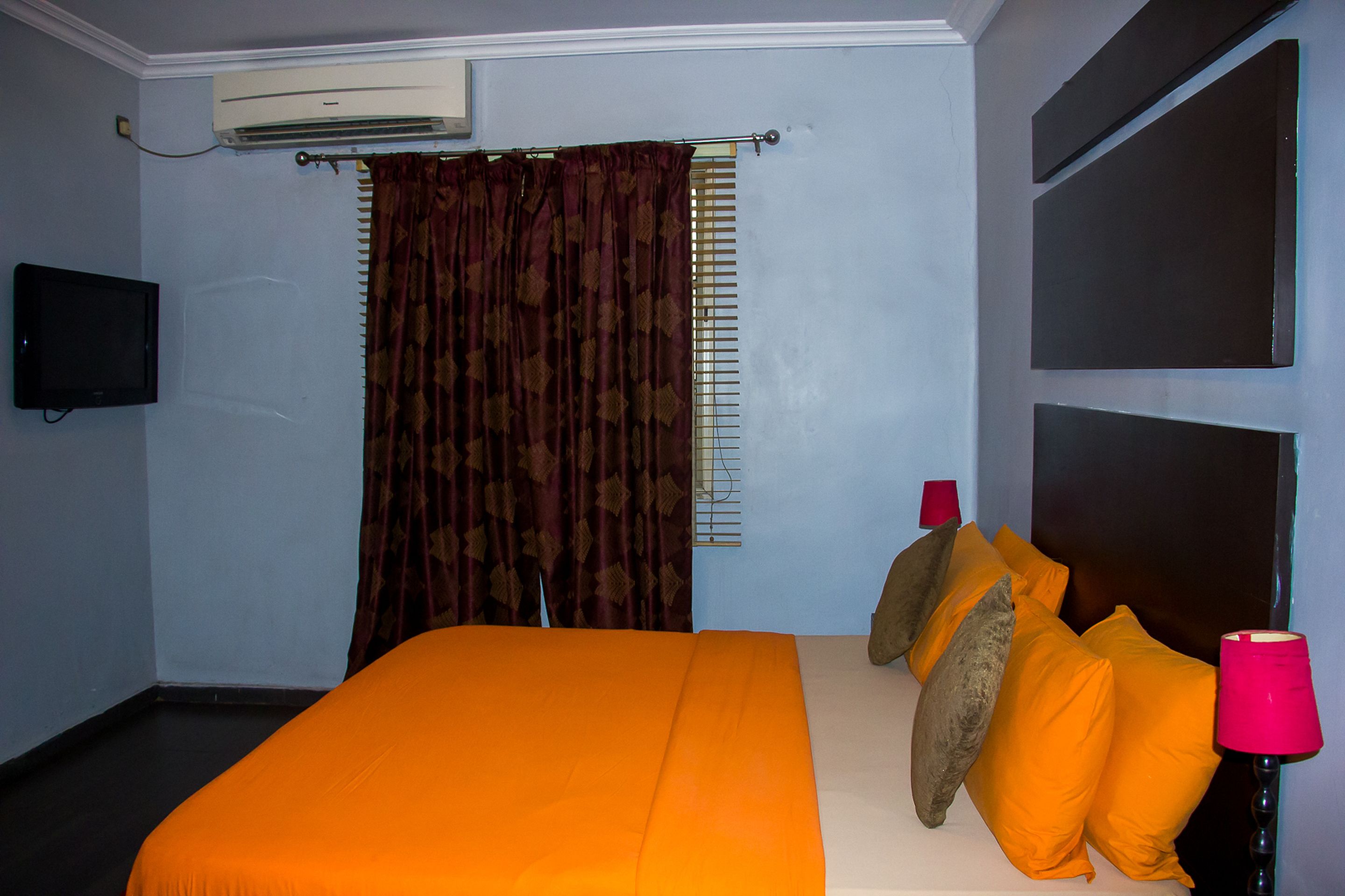 Een hotelkamer met een bed, airconditioning, een televisie en een raam met gordijnen.