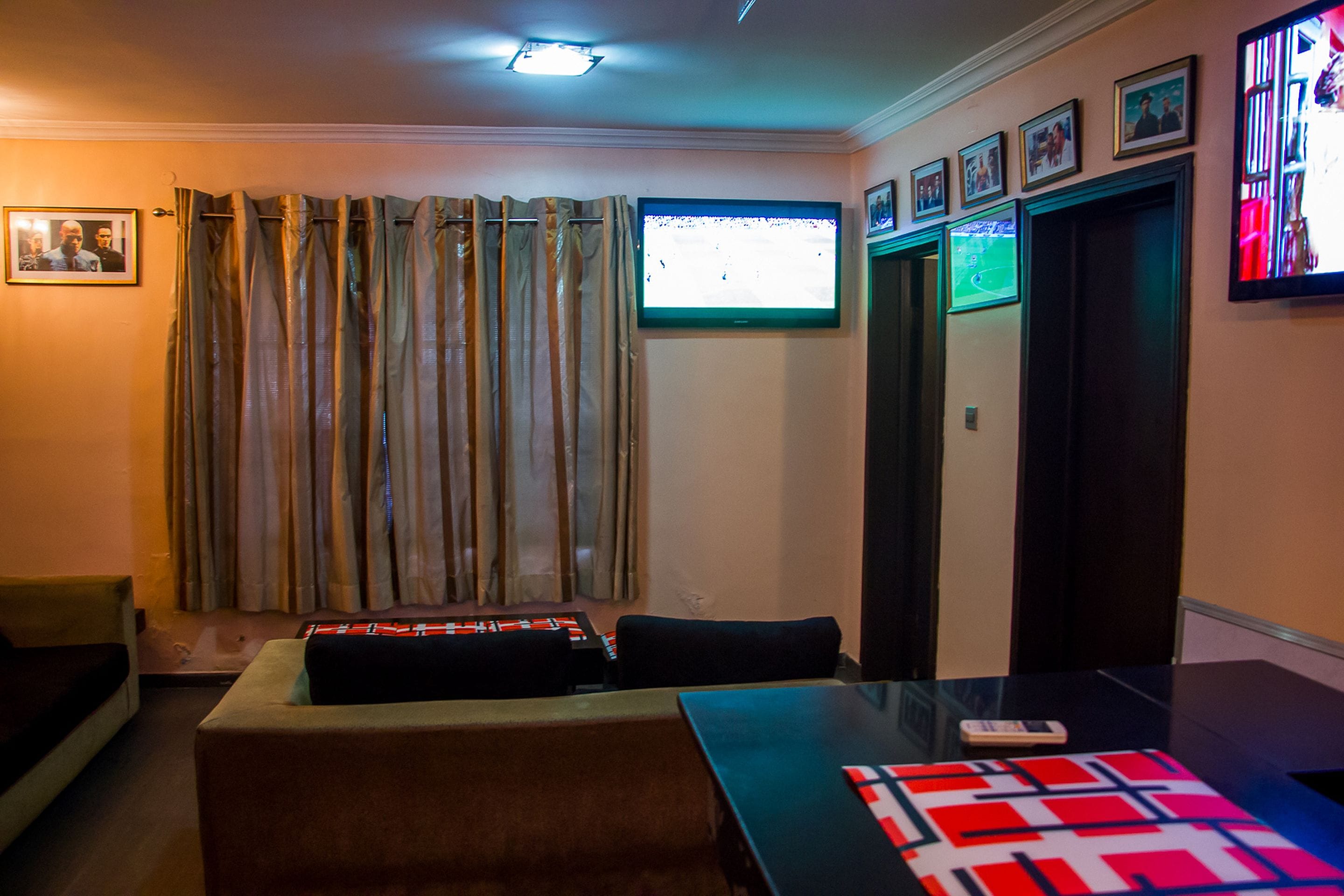Een woonkamer met een flatscreen televisie aan de muur, een bank, een salontafel en een gordijn.