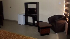 A living room with a white refrigerator, a black entertainment unit, a brown leather chair, and a small wooden table. - The Venetian Suites (Abuja)