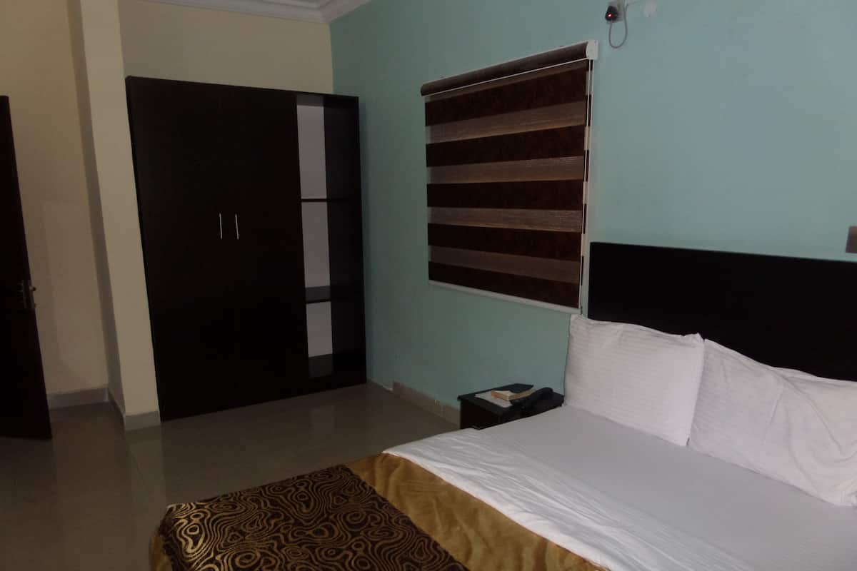 A bedroom with a bed, a nightstand, a wardrobe, and a window with blinds.