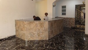 A reception area with a marble counter, a chandelier, and a staircase in the background. - The Venetian Suites (Abuja)