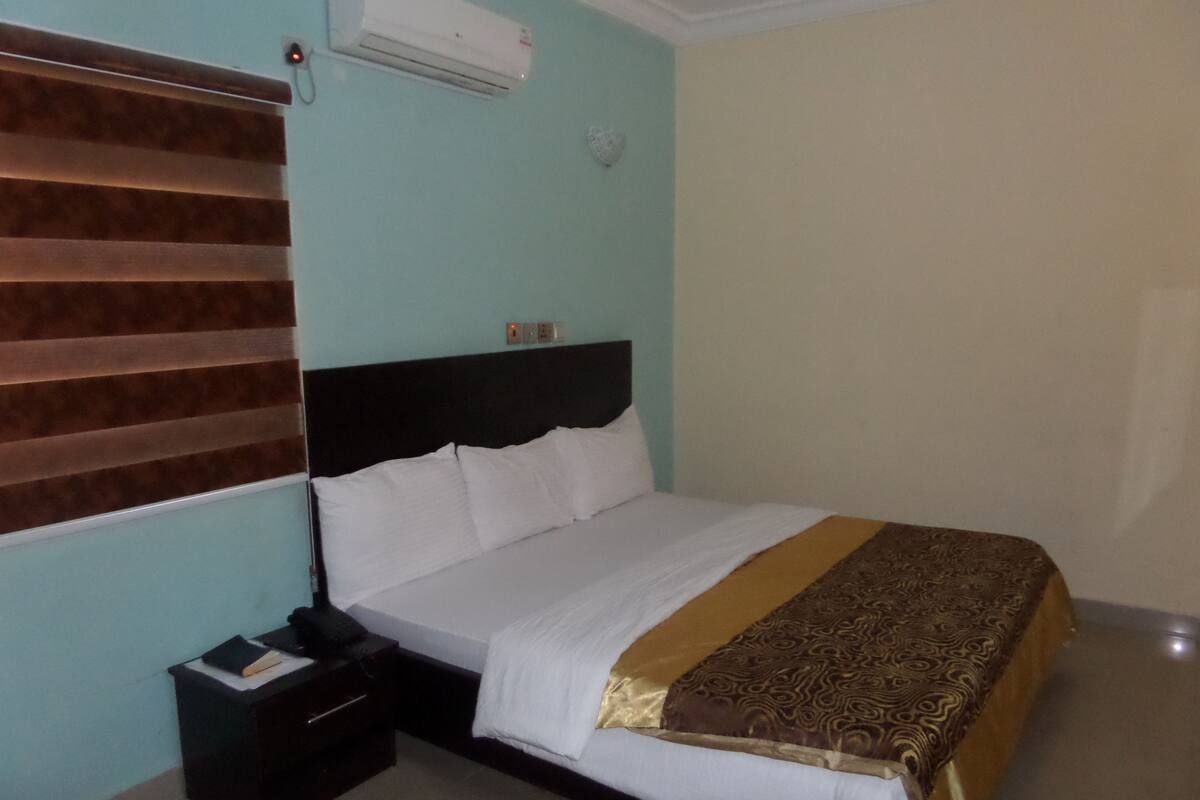 A hotel room with a bed, bedside table, and an air conditioning unit.