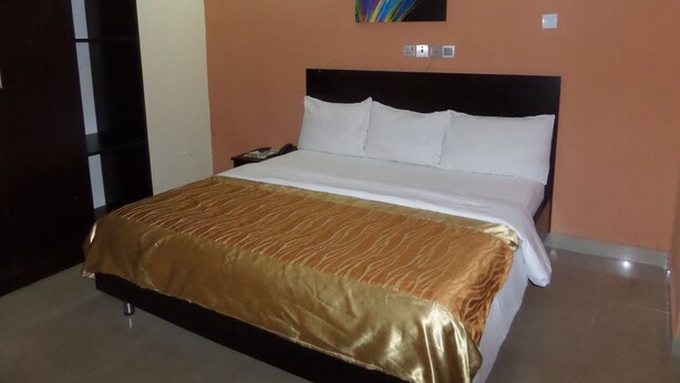 A hotel room with a bed, a nightstand, a telephone, and a wall-mounted painting. - The Venetian Suites (Abuja)