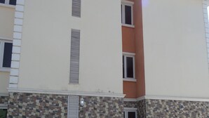 A multi-story building with a stone facade, a flat roof, and a small entrance with a door. - The Venetian Suites (Abuja)