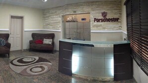 A reception area with a stone wall, a reception desk, two armchairs, and a patterned rug. - Porschester Hotel and Suite (Lagos)