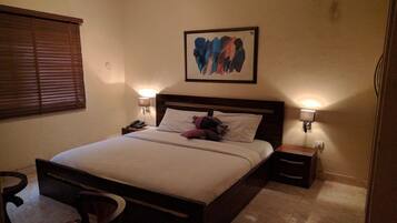 A hotel room with a bed, bedside lamps, a nightstand, a chair, and a painting on the wall.