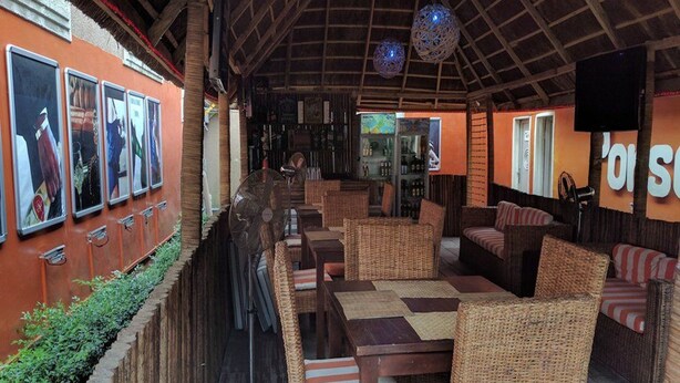 A restaurant with wicker furniture, a long counter, and a wooden ceiling. - Porschester Hotel and Suite (Lagos)