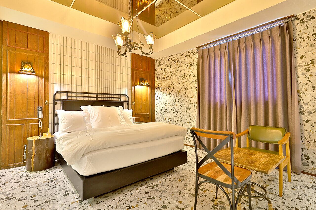 A hotel room with a bed, a chair, a chandelier, and a window with curtains.
