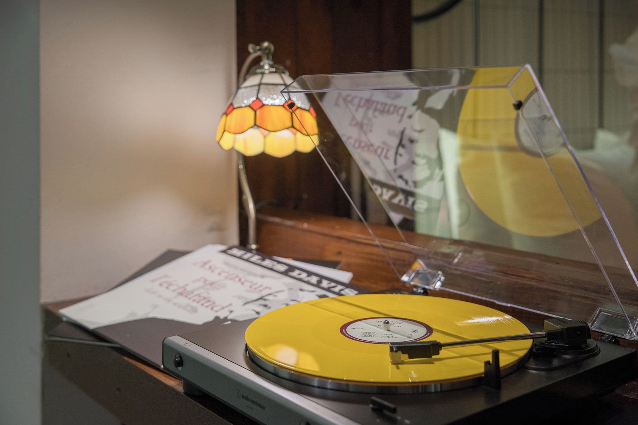 A turntable with a yellow record, a lamp, and papers on a table.