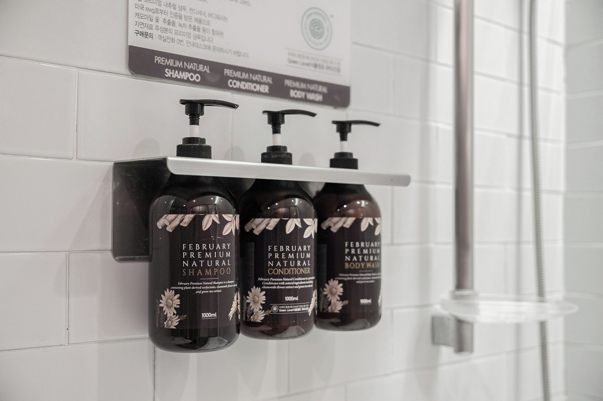 En badevægsflade med tre flasker af February Premium Natural Shampoo, Conditioner og Body Wash.