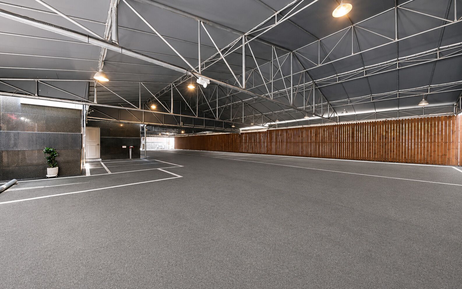 An indoor parking area with a concrete floor, metal beams, and a wooden fence.