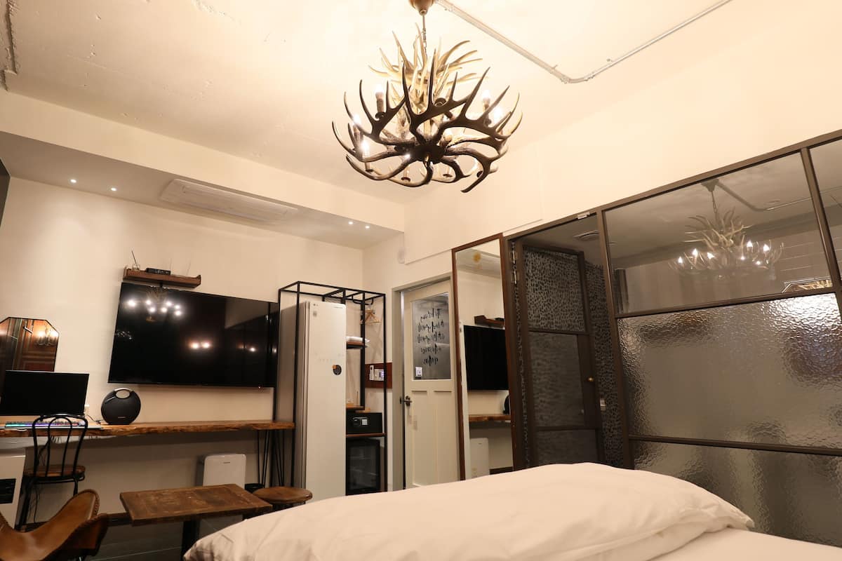 A modern hotel room with a large bed, a desk with a computer, a TV, and a unique antler chandelier.