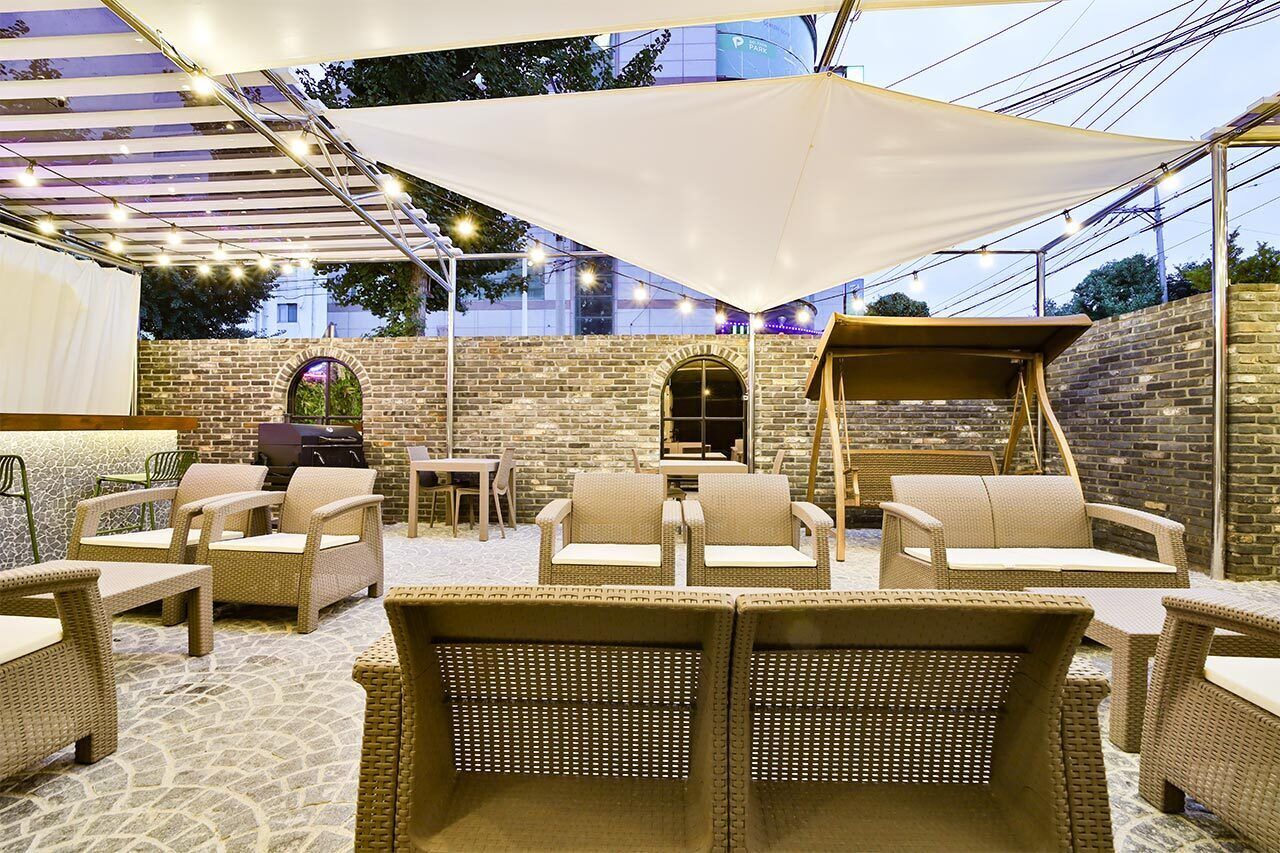 An outdoor patio with wicker furniture, a barbecue grill, and a brick wall backdrop.