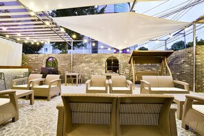 An outdoor patio with wicker furniture, a barbecue grill, and a brick wall backdrop. - February Hotel Sungseo (Daegu)