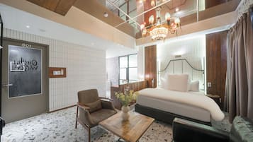 A hotel room with a bed, a seating area, a desk, and a chandelier.