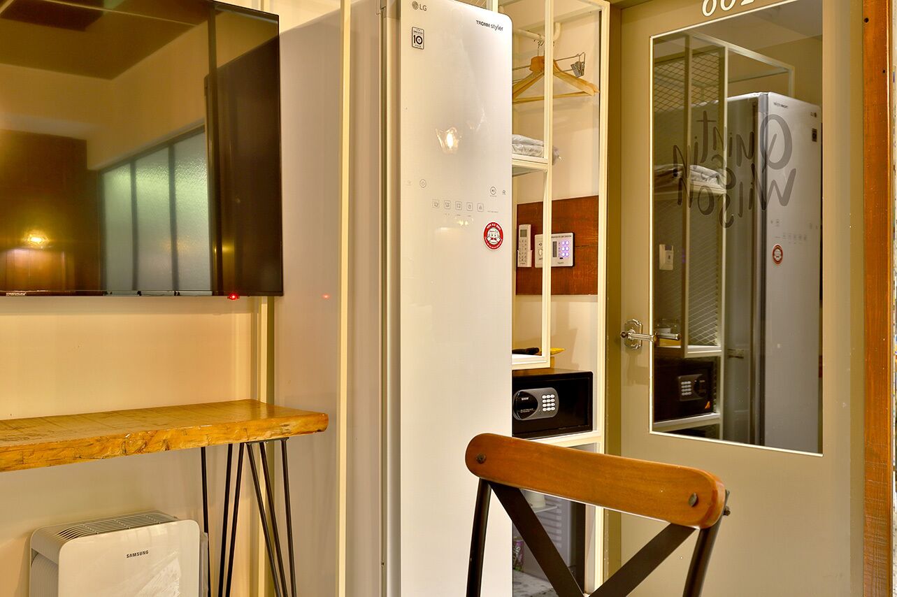 Une pièce avec un climatiseur blanc, une chaise en bois, un téléviseur et une porte donnant sur une salle de bain.