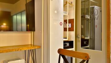 Une pièce avec un climatiseur blanc, une chaise en bois, un téléviseur et une porte donnant sur une salle de bain.